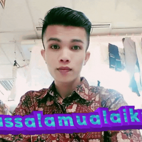 a man in a floral shirt is standing in front of a sign that says ' selamat aik '