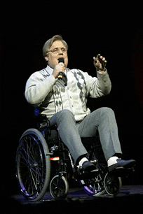 a man in a wheelchair singing into a microphone on a stage