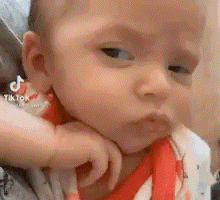 a close up of a baby making a funny face with his hand on his chin .