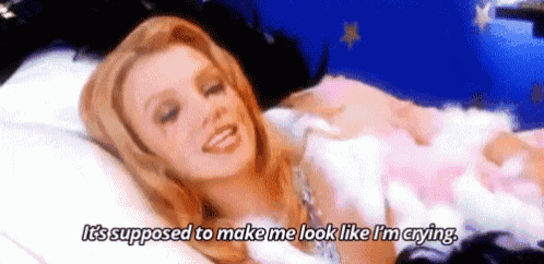 britney spears is laying on a bed with a stuffed animal and crying with tears on her face .