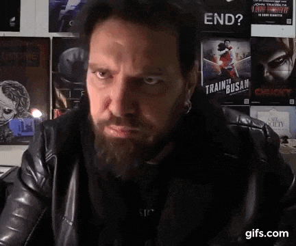 a man with a beard is sitting in front of a wall with posters on it including one that says end