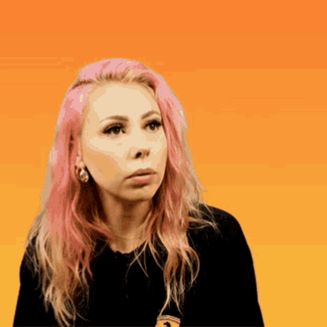 a woman with pink hair is wearing a black shirt with an orange background