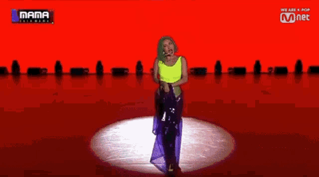 a woman in a neon yellow top is singing on a stage with a mnet logo behind her