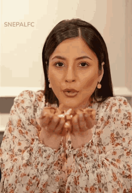 a woman in a floral dress is blowing a kiss while holding something in her hands