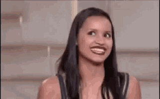 a woman with long black hair is laughing with her mouth open in a close up .