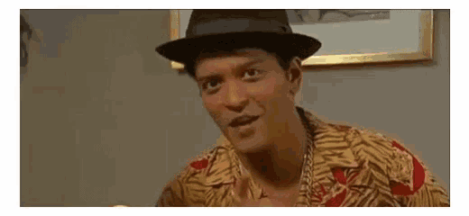 a man in a hat and hawaiian shirt is sitting at a table .