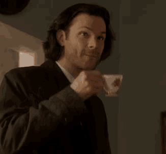 a man in a suit is drinking from a cup