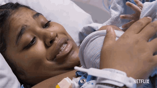 a woman is laying in a hospital bed holding a baby and a netflix logo is visible behind her