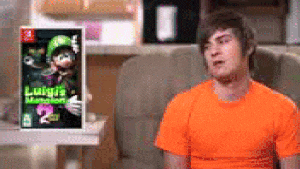 a man in an orange shirt is sitting in front of a luigi 's mansion 2 game .