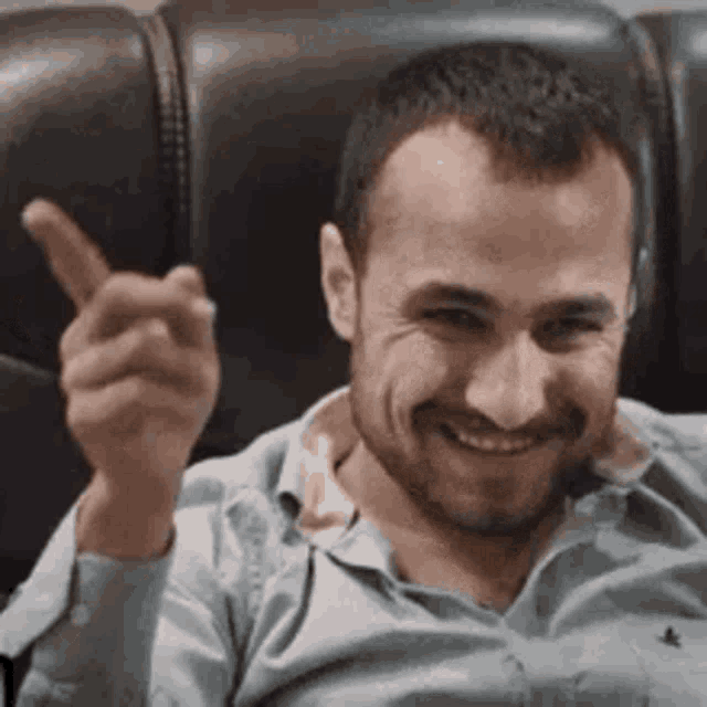 a man is sitting on a couch and smiling while giving a thumbs up .
