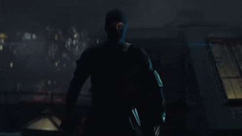 a man in a black mask is standing in the dark holding a gun .