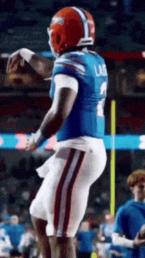 a football player in a blue and red uniform is standing on a field with his arms outstretched .