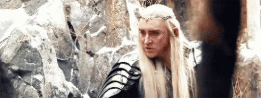 a man with long white hair and a crown is standing next to a rock wall .