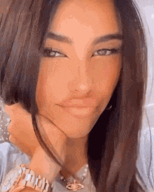 a close up of a woman 's face with her hand on her chin . she is wearing a watch and a necklace .