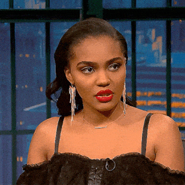 a woman wearing red lipstick and earrings looks at the camera with a serious look on her face