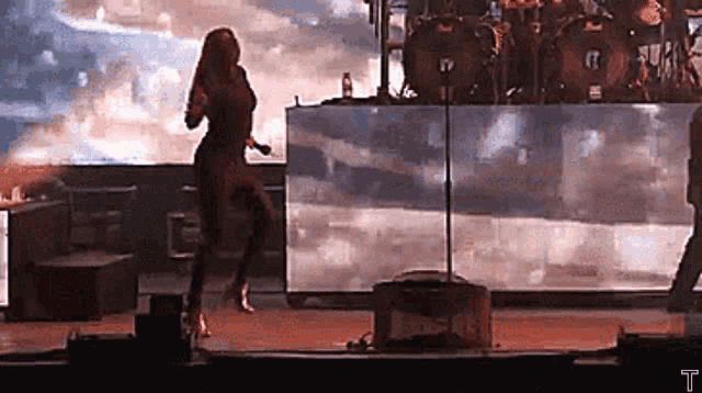a woman is dancing on a stage in front of a drum set and a microphone .