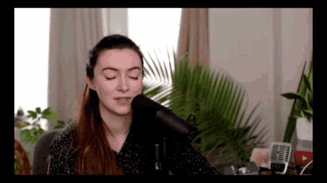 a woman singing into a microphone with her eyes closed in front of a palm tree