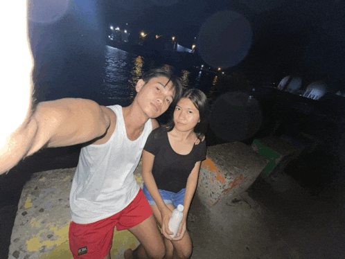 a man in a white tank top and red shorts is taking a selfie with a girl