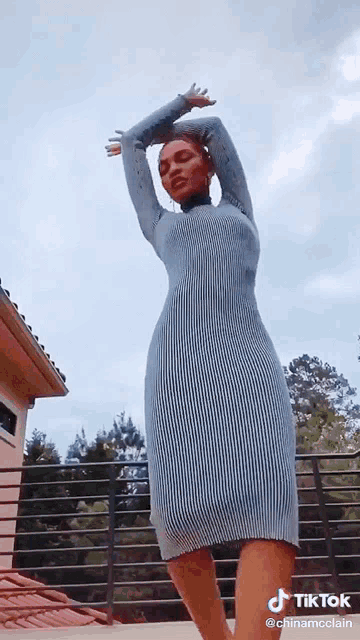 a woman in a blue dress is standing on a balcony with her arms in the air .