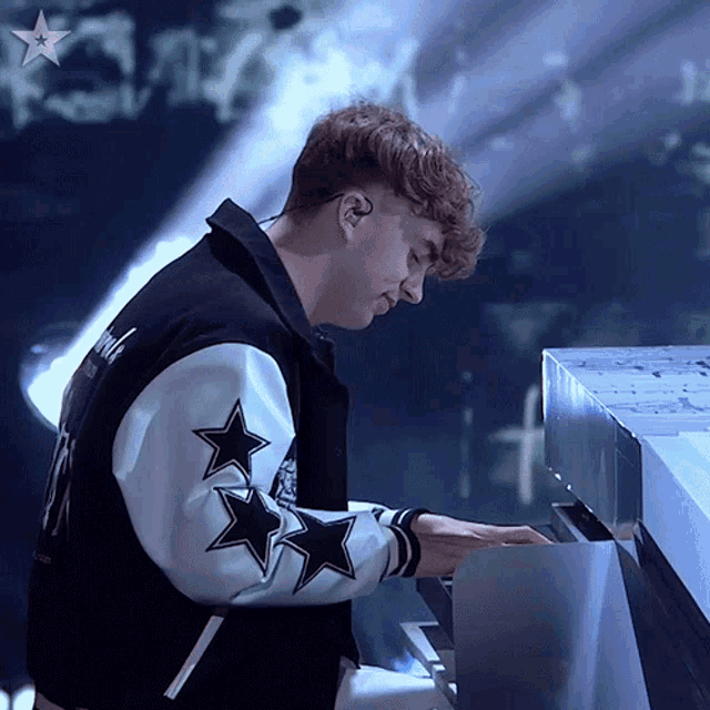 a man in a varsity jacket with stars on the sleeves plays a piano