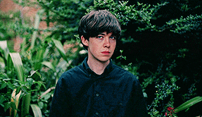 a young man in a black shirt is standing in front of trees