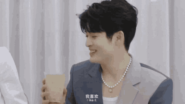 a young man wearing a pearl necklace and a suit is holding a glass of liquid .