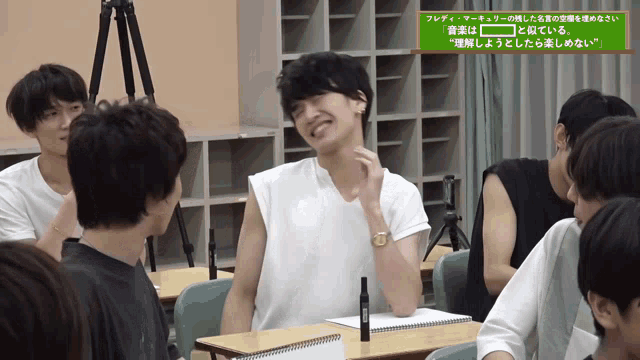 a group of young men are sitting in a classroom with a green sign that says " フレディ マーキュリー "