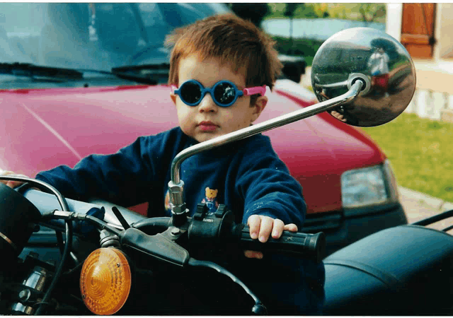 a young boy wearing sunglasses is riding a motorcycle