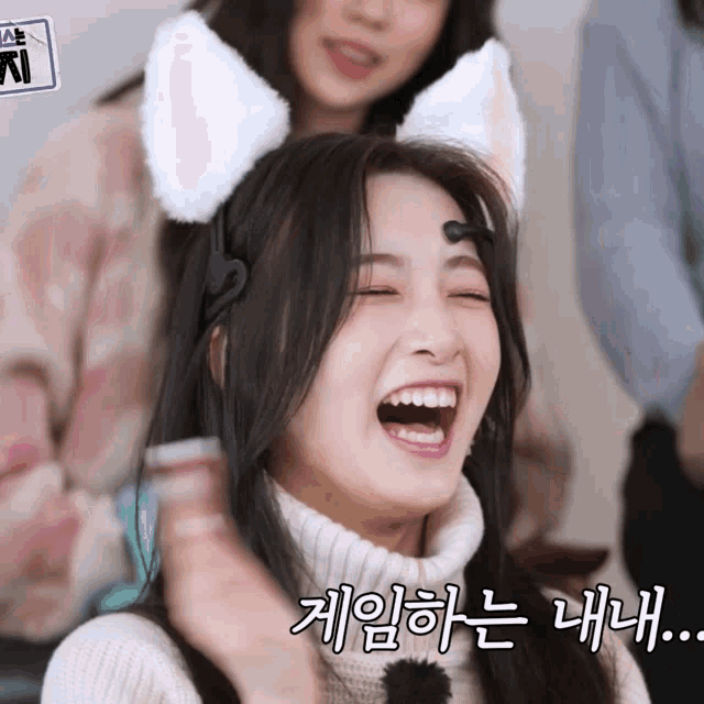 a woman wearing a cat ear headband is laughing with korean writing behind her