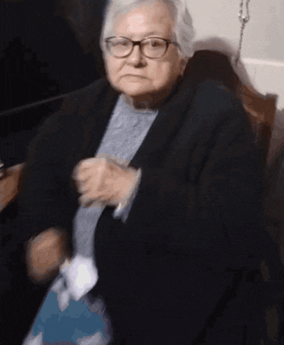 a woman wearing glasses and a black jacket is sitting in a chair
