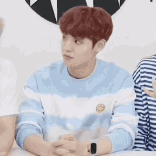 a young man with red hair is wearing a blue and white striped sweater and a watch .