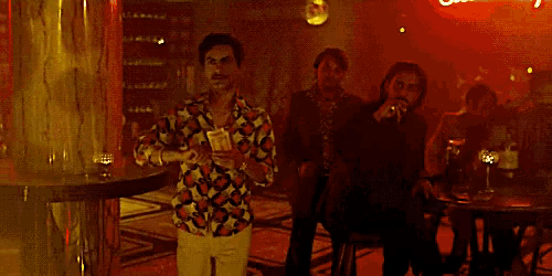 a man in a colorful shirt is holding a bunch of money in a dark room