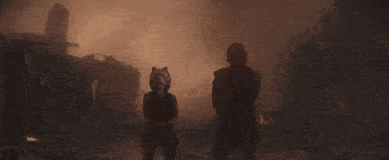 a man and a woman are standing in front of a fire in a dark room .