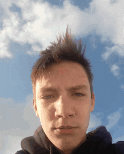 a young man with a mohawk takes a selfie with a blue sky in the background