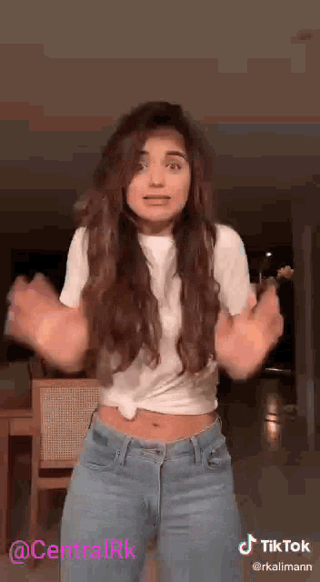 a woman in a white t-shirt and blue jeans is dancing in a living room .