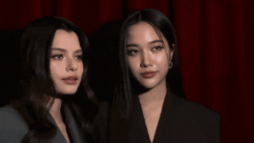 two women standing next to each other with a red curtain in the background