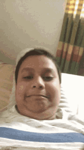 a man is laying on a bed with a striped blanket and making a funny face