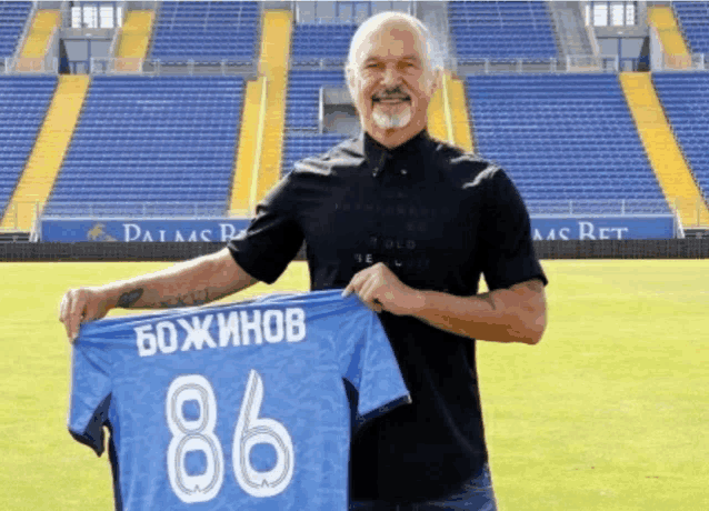 a man in a black shirt holds up a blue shirt with the number 86 on it