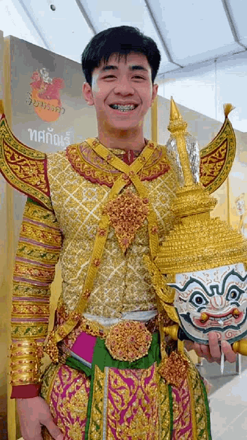 a man in a costume holds a mask in front of a sign that says ' thailand ' on it