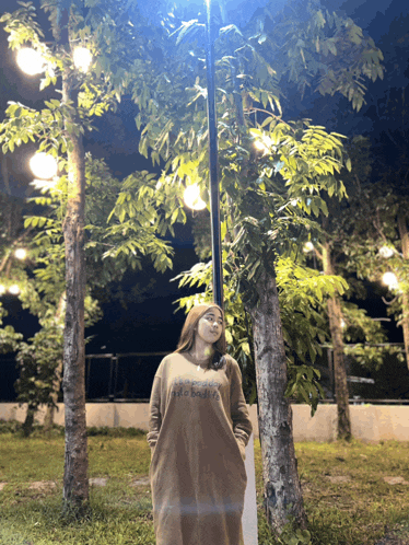 a woman in a brown dress with the word brooklyn on it stands in front of trees