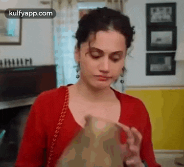 a woman in a red shirt is standing in a room and holding a book .