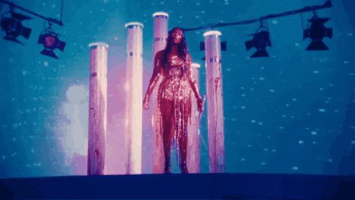 a woman in a gold dress is standing in front of a row of pillars