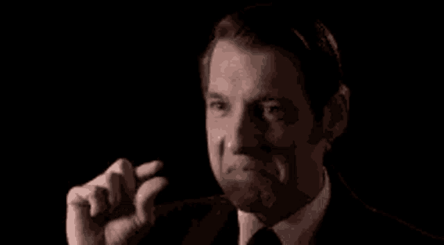 a man in a suit and tie is covering his face with his hand in a dark room .