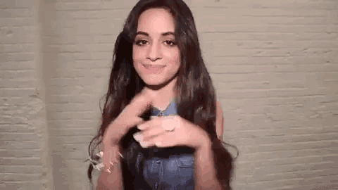 a woman with long hair is making a heart with her hands .