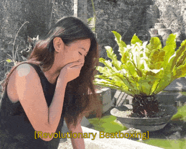 a woman laughs in front of a plant with revolutionary beatboxing written in yellow