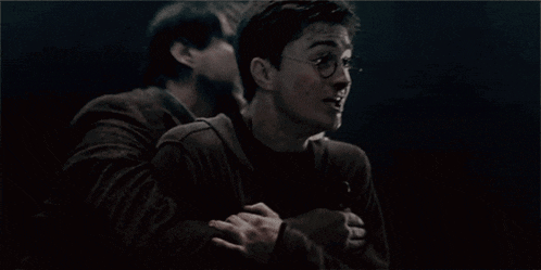 two men are hugging each other in a dark room and one of them is wearing glasses .