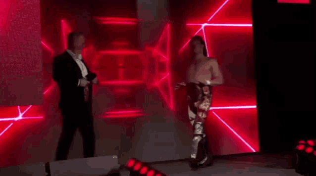 a man in a suit is standing next to a wrestler on a stage holding a belt .