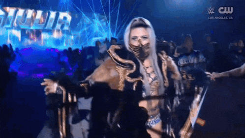 a woman in a mask is walking through a crowd in a wrestling ring .