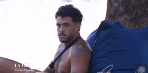 a shirtless man sits on a blue bean bag chair with la villa on the bottom
