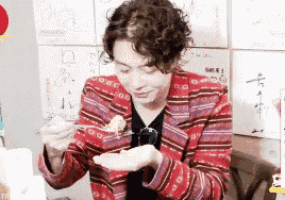 a man in a striped jacket is eating food with a fork and spoon .